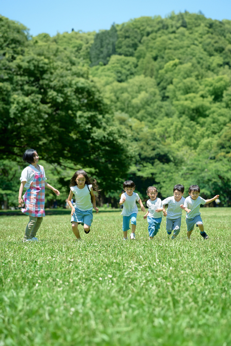 Children running in a green field and a Japanese woman watching over them (People)