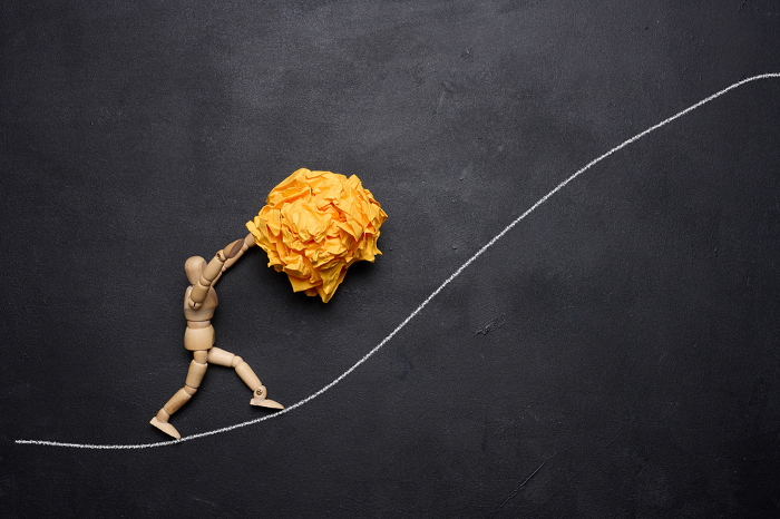 A wooden figurine of a person rolling a crumpled paper ball upwards, concept of perseverance and hard work, achieving goals. A wooden figurine of a person rolling a crumpled paper ball upwards, concept of perseverance and hard work, achieving goals.