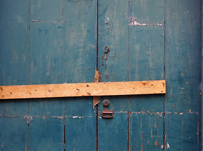 close up of an old peeling green painted wooden plank door barred shut with a piece of timber and rusty nails with a lock and handle close up of an old peeling green painted wooden plank door barred shut with a piece of timber and rusty nails with a lock and handle