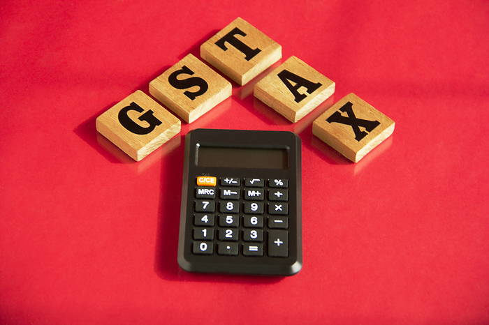 GST and TAX wooden letters words with calculator on a red background, financial concept. GST and TAX wooden letters words with calculator on a red background, financial concept.