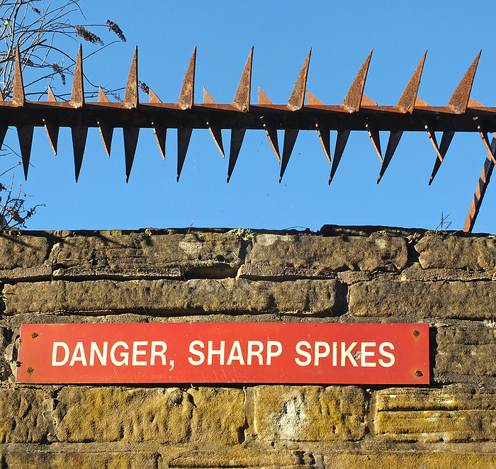 rusty iron sharp spikes on the top of an old stone wall with a red danger sign against a blue sky rusty iron sharp spikes on the top of an old stone wall with a red danger sign against a blue sky