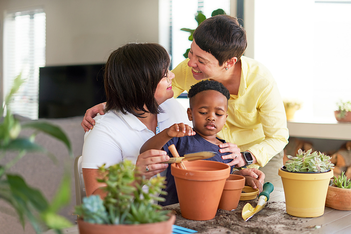 Happy lesbian couple and son planting plants in flowerpots at home