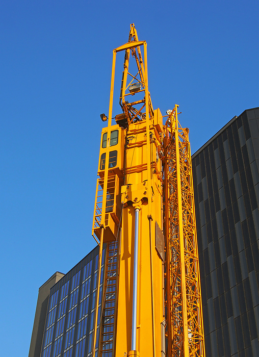 a folded yellow construction crane with gantry strapped to the side waiting to be deployed on an urban building site a folded yellow construction crane with gantry strapped to the side waiting to be deployed on an urban building site