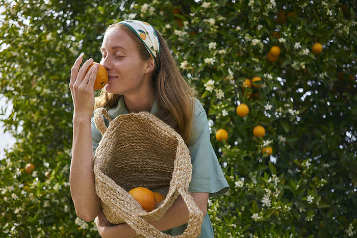 Woman smelling orange holding basket in orchard