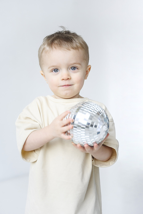 Cute boy holding disco ball against white background