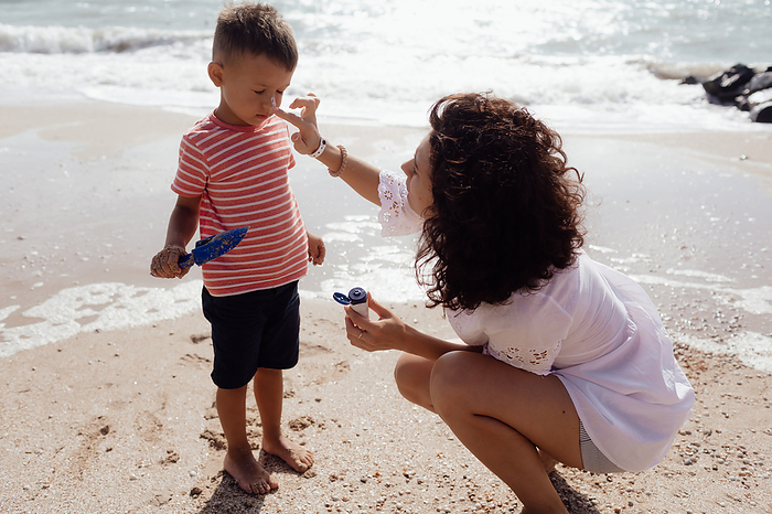 Caring mom smears sun cream on her son on the seashore