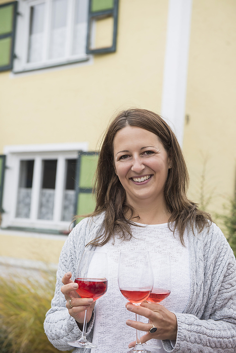 Woman holding three glasses of wine, good host Mid adult woman holding three glasses of red wine, Bavaria, Germany