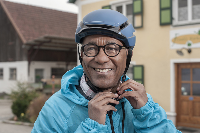 man is fixing a bike helmet,e bike,pedelec,health,environmental consciousness Senior man fastening on bicycle helmet and smiling, Bavaria, Germany