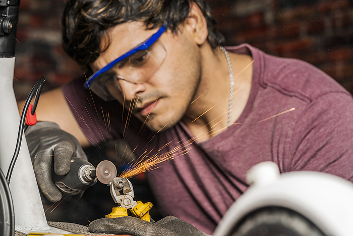 A mechanic wearing safety goggles using a mini grinder to cut a screw