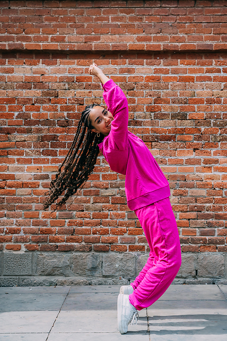 Smiling woman dancing in front of brick wall