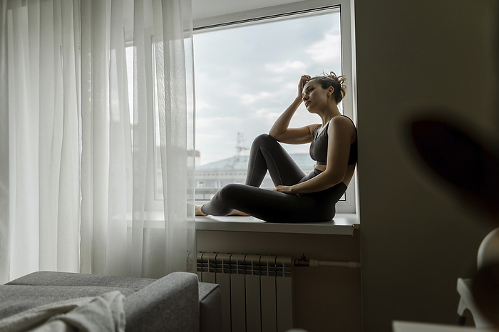 Thoughtful woman relaxing on window sill at home