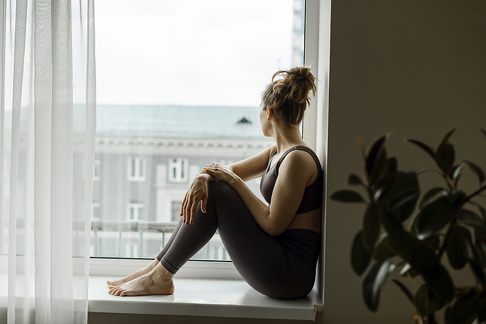 Thoughtful woman looking out of window sitting at home