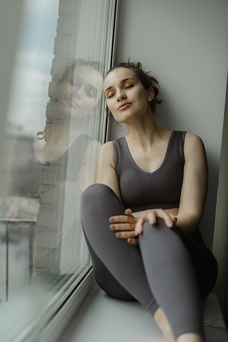 Woman with eyes closed relaxing on window sill at home
