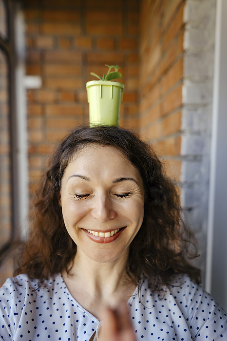 Happy woman meditating with potted plant on head