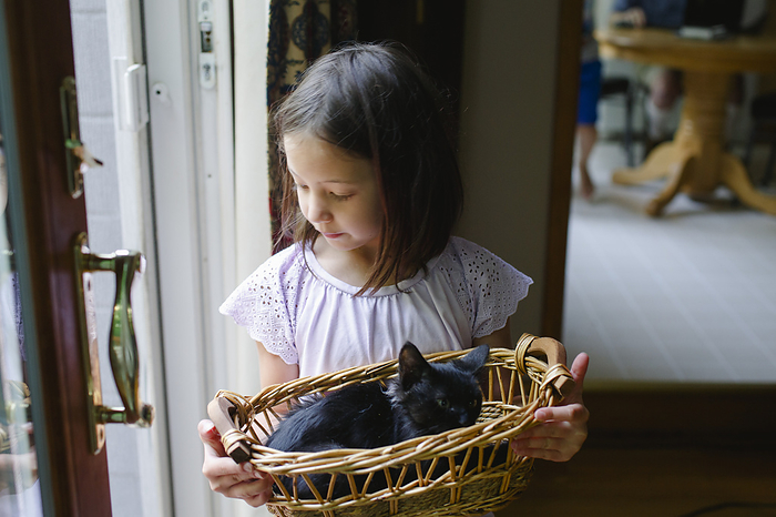 Little girl stands at a large glass door with a small kitten in basket
