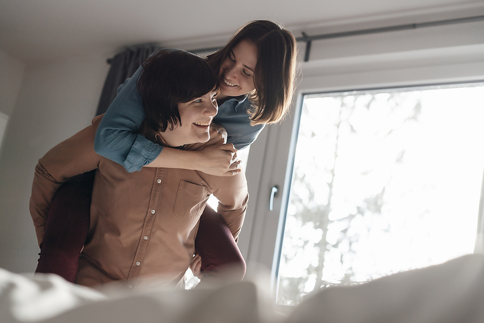 Smiling woman piggybacking lesbian friend at home