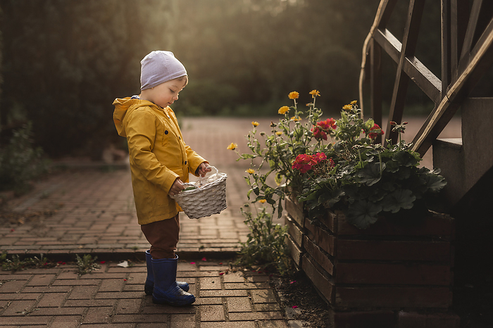 Boy in yellow raincoat and blue wellingtons holding white basket