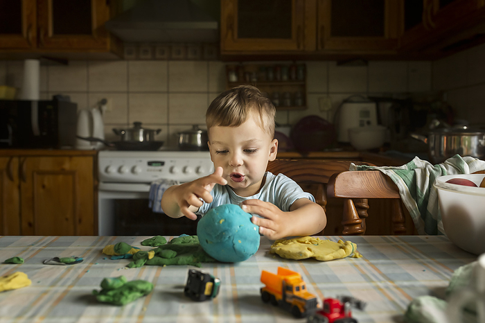Blonde boy playing on kitchen table with colorful play doh and c