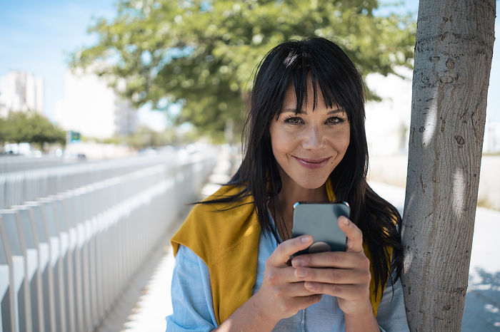 Smiling businesswoman with bangs holding mobile phone