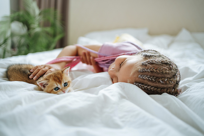 Girl playing with ginger kitten on bed