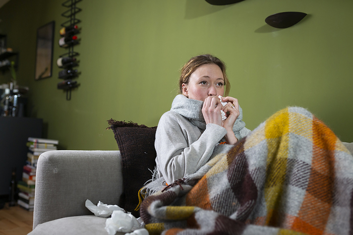 Young woman laying on the couch is sick Sick young woman blowing nose with tissue relaxing on couch