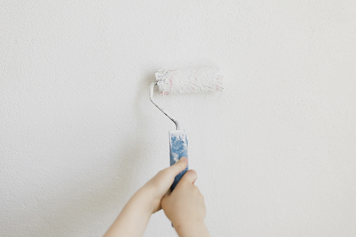 Hand of boy painting white wall using roller at home