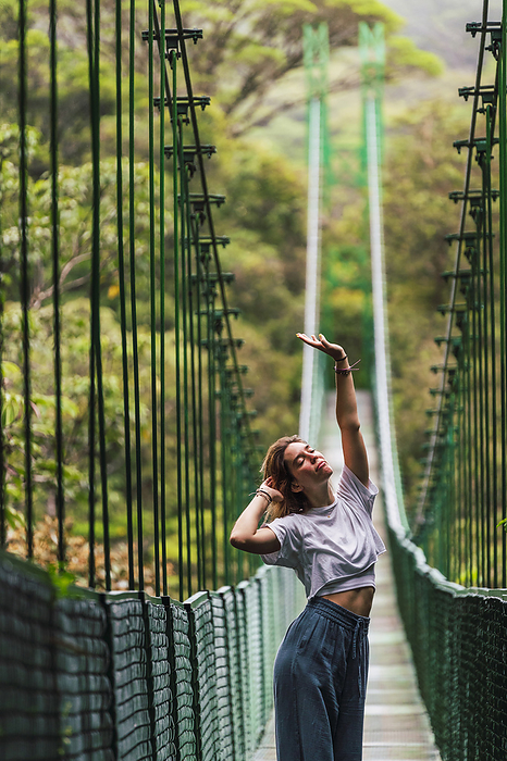 Woman with hand raised standing on suspension bridge