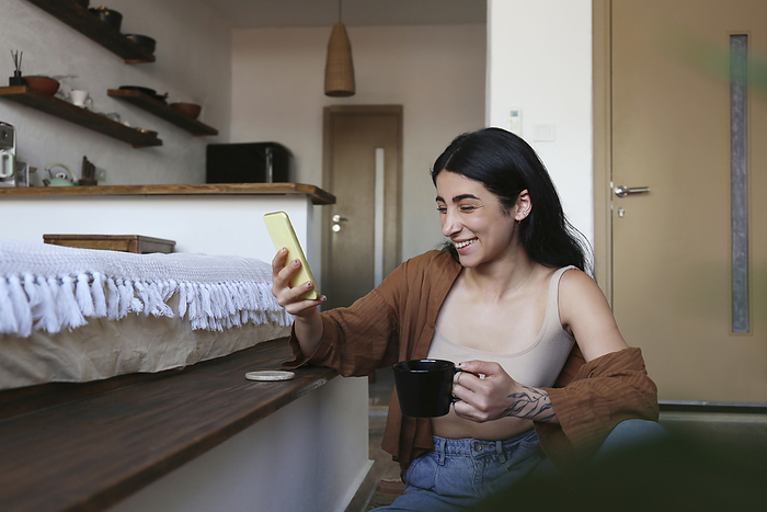 Happy young woman on video call enjoying coffee at home