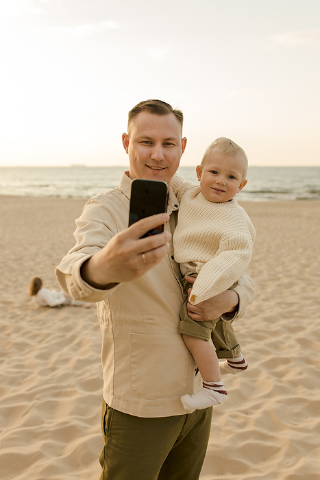 Smiling man taking selfie with son at beach
