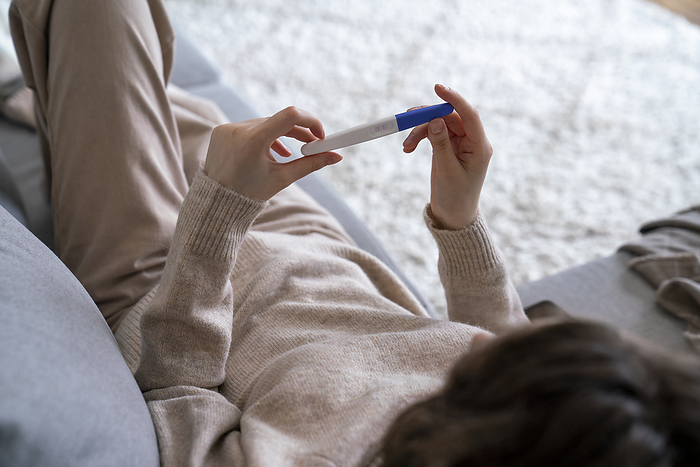 Woman holding pregnancy testing kit relaxing on sofa