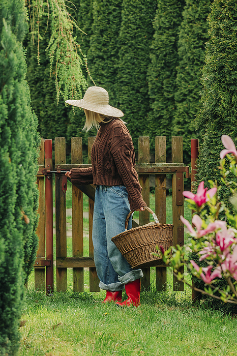 Woman with basket full of logs closing gate in garden