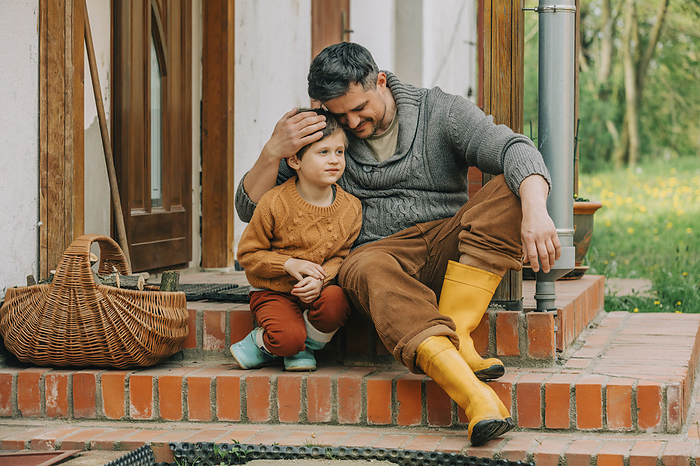 Father embracing son sitting on steps of house