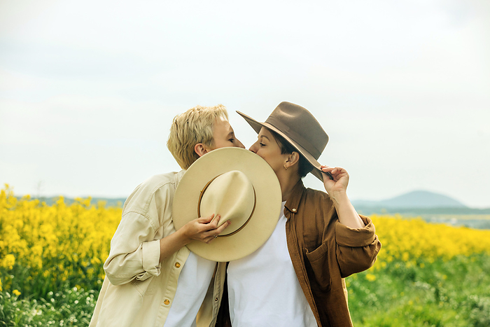 Lesbians wearing cowboy hat kissing each other at field