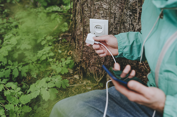 Man inserting mobile phone charger in outlet on tree trunk