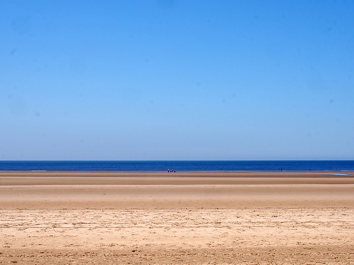 a long sandy beach with blue summer sky and blue sea with a group distant unidentifiable people near the water a long sandy beach with blue summer sky and blue sea with a group distant unidentifiable people near the water