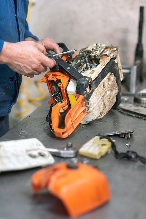 Mechanic repairing a chainsaw. Man repairing a chainsaw in workbench. Mechanic repairing a chainsaw. Man repairing a chainsaw in workbench.