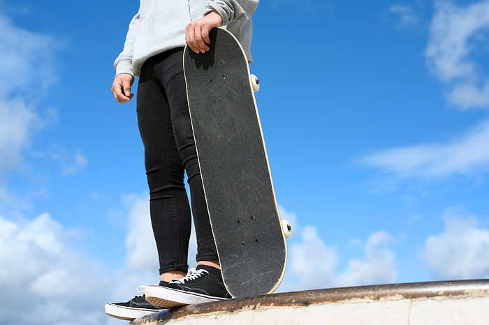 Close up of unrecognizable young man holding skateboard in the park on blue sky background. Close up of unrecognizable young man holding skateboard in the park on blue sky background.