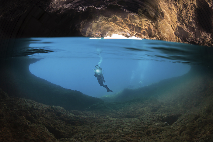Half above, half below shot of a diver at the entrance to a cavern that breaks the surface on the island of Gato, Bohol Sea, Philippines, Southeast Asia; Gato, Philippines, by Dave Fleetham / Design Pics