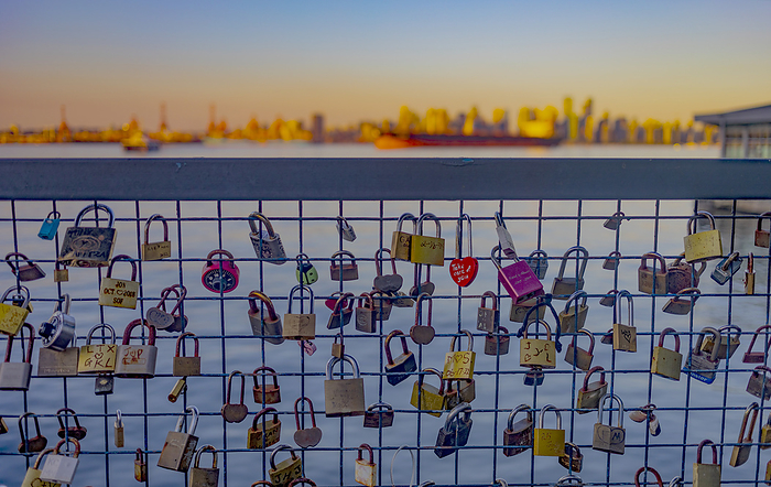Love locks on a waterfront railing in the foreground on the Quay in North Vancouver with a blurred distant view of the downtown Vancouver skyline at dusk; Vancouver, British Columbia, Canada, by Lorna Rande / Design Pics
