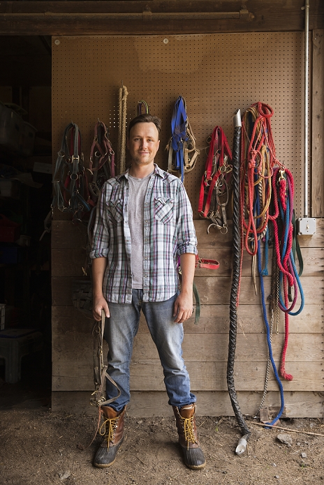 An organic farm in the Catskills. A man standing in a tack room in a stable.