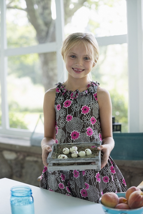 A young girl in a floral dress, examining a clutch of speckled bird eggs in a box.