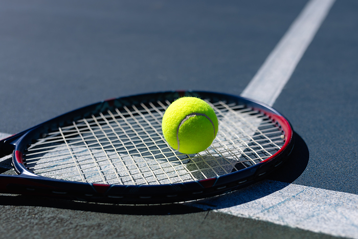 Close up of tennis ball and tennis racket lying on tennis court on sunny day, copy space. Sport, sports equipment and active lifestyle.