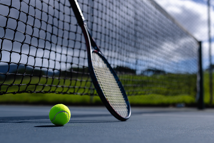 Close up of tennis ball and tennis racket against net on tennis court on sunny day, copy space. Sport, sports equipment and active lifestyle.