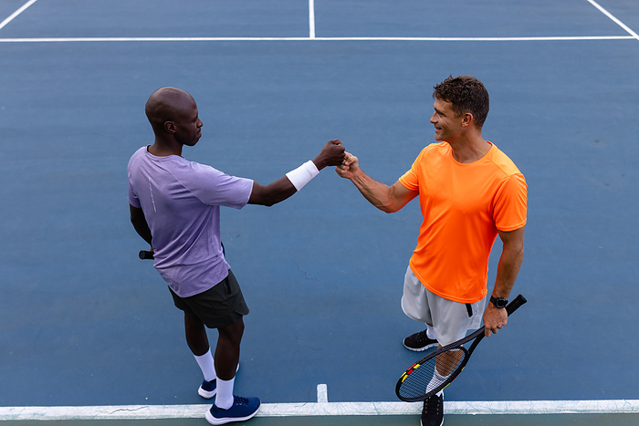 Diverse male tennis players fist bumping, playing doubles on outdoor court. Sport, competition, hobbies, teamwork and active lifestyle, unaltered.