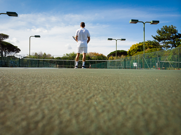 Low angle rear view of caucasian male tennis player playing on sunny outdoor court, copy space. Sport, competition, hobbies and active lifestyle.