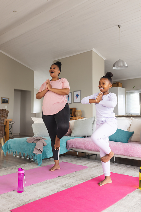 Happy african american mother and daughter doing yoga and meditating in living room. Motherhood, togetherness, relaxation, childhood, active lifestyle and domestic life, unaltered.