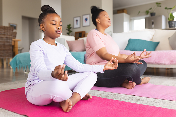African american mother and daughter doing yoga and meditating in living room. Motherhood, togetherness, relaxation, childhood, active lifestyle and domestic life, unaltered.