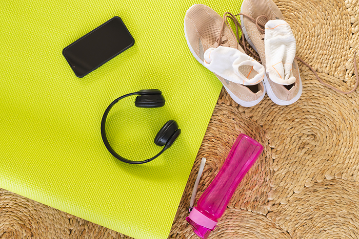 Sports equipment with yoga mat, sports shoes, plastic bottle, smartphone and headphones on carpet. Sport, technology and activity.