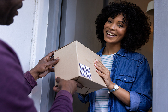 Happy biracial woman receiving parcel at home. Lifestyle, free time, online shopping and domestic life, unaltered.