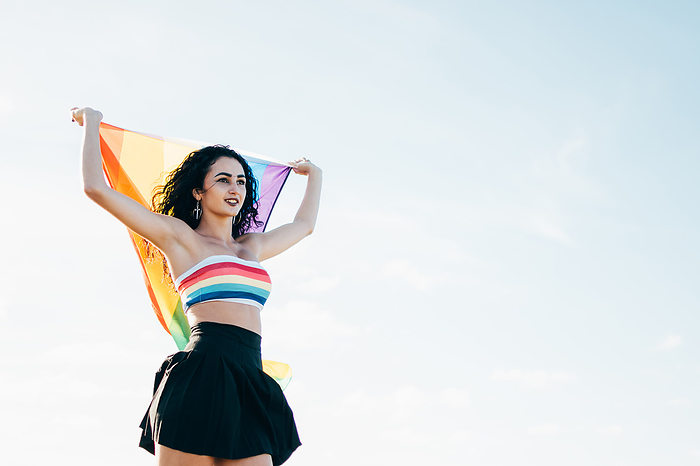 Young woman holding a lgbt flag from behind. Dressed in a colorful top